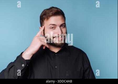 Man in black shirt making a thinking gesture against blue background. Stock Photo
