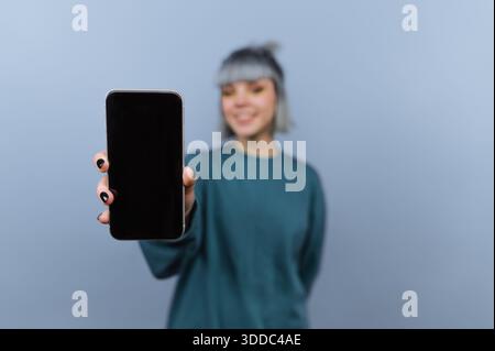 Person holding a smartphone with a blank screen against a blue background. Stock Photo