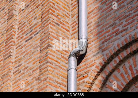 brickwork creating a distinct pattern on the corner of a building, featuring a curved downpipe and sunlit texture Stock Photo