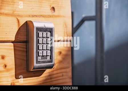 Electronic numeric keypad for door access control system, ensuring security and authorized entry on a textured wooden wall Stock Photo