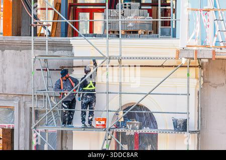 31 October 2025, Tbilisi, Georgia: Two construction workers applying paint to a building facade while standing on scaffolding, performing renovation Stock Photo