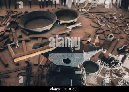 Anvil and hammer lying on a blacksmith's workbench, surrounded by various traditional metalworking tools and old horseshoes Stock Photo