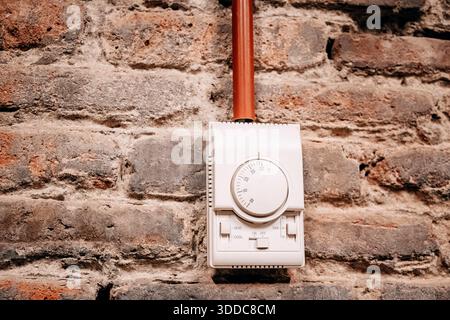 Modern white thermostat controlling climate and heating system, mounted on a textured, rustic red brick wall Stock Photo