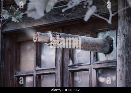 Exhaust pipe protruding from a broken window in a vintage wooden building, representing DIY heating and rustic ventilation Stock Photo
