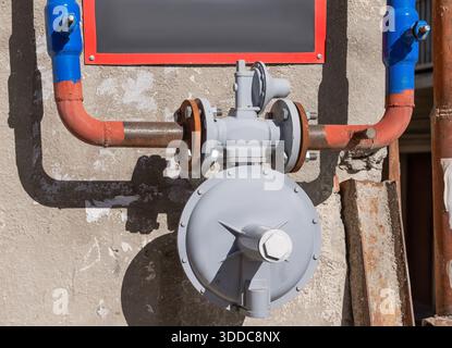 Gas piping system featuring a pressure regulator, valves, and rusty pipes on an old building wall Stock Photo