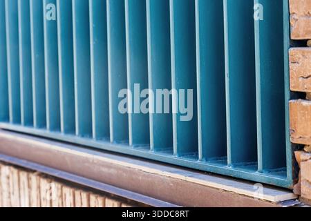 Blue metal bars forming a fence or grate, creating a strong vertical pattern alongside warm brickwork on a building exterior Stock Photo