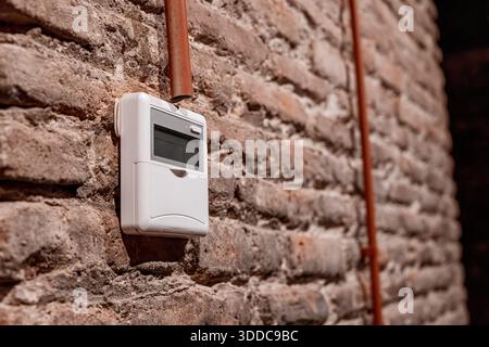 Modern digital thermostat mounted on an old rustic brick wall, displaying fan speed settings for climate control Stock Photo