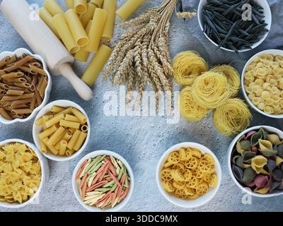 Composition with different tasty uncooked pasta and bundle of wheat. Italian pasta wallpaper, different types and shapes of pasta layout Stock Photo