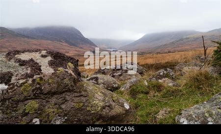 Ogwen valley landscape with large rocks in the foreground, mountains disappearing into mist and a lake far in the distance Stock Photo