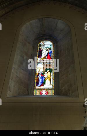 Colorful stained glass window in a stone church wall, illustrating a biblical scene with figures in vibrant robes. The warm light enhances sacred atmo Stock Photo