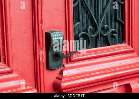 Red wooden door featuring a modern electronic keypad lock and handle, providing keyless entry and enhanced security for a smart home Stock Photo