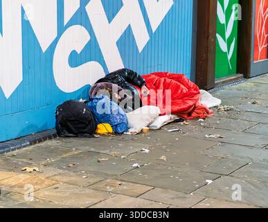 Bristol UK 12-29-2025 A homeless person sleeps on the sidewalk, wrapped a blanket. The scene highlights urban poverty Stock Photo