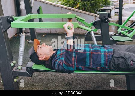 Man doing a chest press workout on green outdoor fitness equipment, at a public park Stock Photo