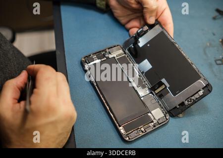 Man Works on Repairing a Smartphone Inside a Workshop While Tools and Components Are Present on the Table Stock Photo