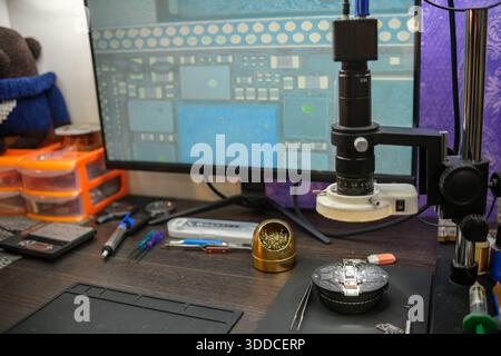 Workspace for Electronic Repair With Tools, Microscope, and Monitor Displaying Circuit Board Design Taken in a Well-Lit Room Stock Photo
