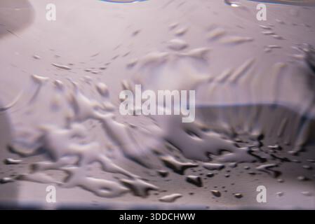 348.An abstract, intense close-up of a liquid surface from a side angle. The composition shows multiple water drops and liquid trails, creating a clea Stock Photo