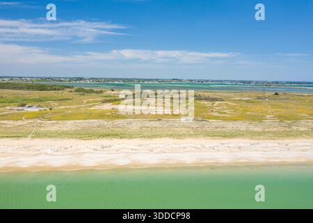 High-angle perspective of Plage du Mentor in Quiberon, featuring pale sandy dunes, greenish coastal water, and a wide lagoon under a clear blue sky. The landscape is open, sunlit, and expansive with soft natural colors. Stock Photo