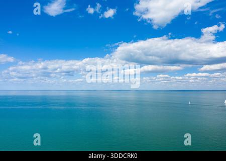 Vast turquoise waters of the Atlantic Ocean stretch to the horizon beneath a sky filled with puffy white clouds. A few small sailboats dot the tranquil scene near Ile de Re, evoking a sense of space and peacefulness. Stock Photo