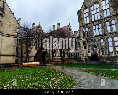 Manchester, UK - December 06, 2025: Courtyard scene on a university campus in Manchester with stone arches, benches, and a dark sculpture. Stock Photo