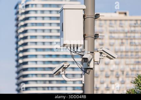 Multiple security cameras fixed on a pole monitoring a city street with modern buildings in the background, focusing on safety and privacy Stock Photo