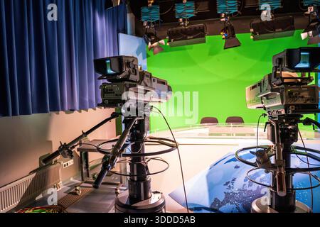 Prague, Czech Republic - May 1, 2023: Two professional cameras on tripods face a bright green screen in a modern news studio, suggesting live broadcas Stock Photo