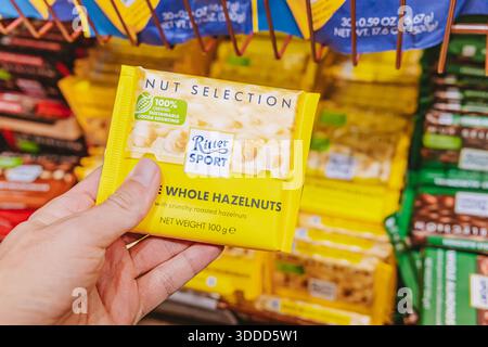 7 November 2025, Tbilisi, Georgia: Hand holding a yellow packaged Ritter Sport whole hazelnuts chocolate bar in a grocery store aisle Stock Photo