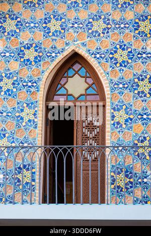 Architectural detail showing a balcony, ornately carved wooden door, and colorful geometric mosaic tile patterns on a building facade Stock Photo