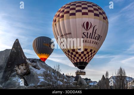 Hot air balloons from Sultan Balloons and Güvercin Balloons rise above rock formations in Göreme, Central Anatolia Region, Turkey. Tuff stone landscape and fairy chimneys Stock Photo