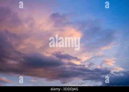 Soft pink and lavender clouds drift across a vibrant blue sky at dusk, creating a gentle and atmospheric scene with subtle gradients of color and light. Stock Photo