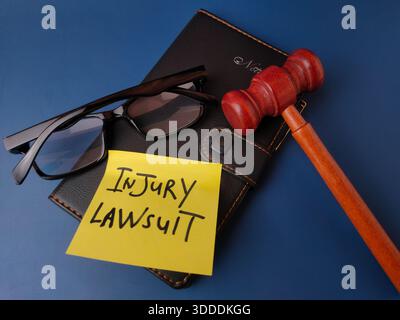 The image displays a legal concept represented by a gavel, glasses, notebook, and a sticky note with the text INJURY LAWSUIT. Stock Photo