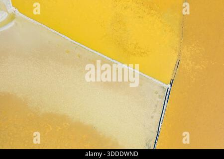 Geometric salt pans in vivid yellow and ochre tones create an abstract pattern at the Missolonghi salt marsh in western Greece. The aerial perspective highlights the sharp lines, mineral textures, and unique coloration of the wetland landscape. Stock Photo