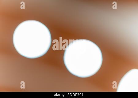 A soft and blurry abstract background featuring bright white circular bokeh spots on a warm orange and brown surface. Stock Photo