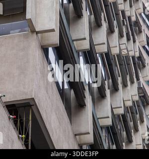 A view from below to top of a building in natural tone colour with glass windows, an extruded wall panel and a bar panel cladding. Stock Photo