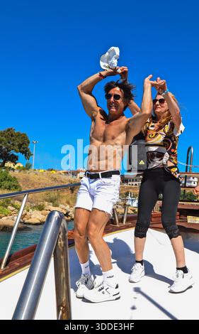 A group of happy people enjoys a lively dance party on a boat deck under a clear blue sky in summer Stock Photo