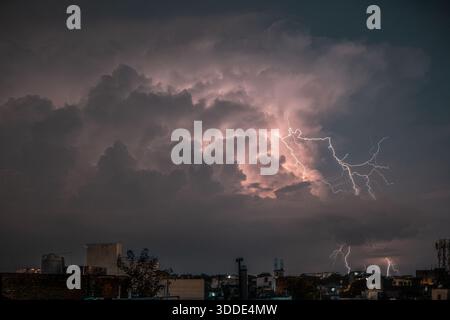 Lightning strikes during a severe thunderstorm over an urban city skyline at night Stock Photo