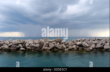 Storm clouds and rain over the sea behind rocky breakwater Stock Photo
