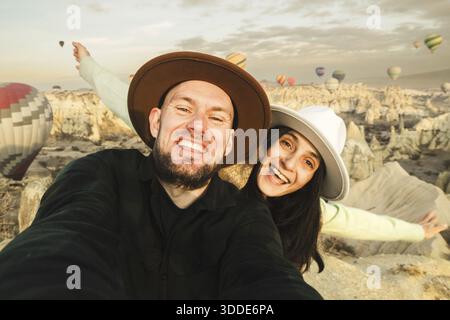 Close up Couple of tourists having fun watching hot air balloons from viewpoint smile to camera in Cappadocia at holiday - Happy friends laughing toge Stock Photo