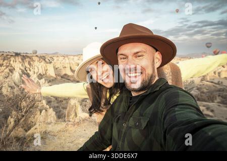 Close up Couple of tourists having fun watching hot air balloons from viewpoint smile to camera in Cappadocia at holiday - Happy friends laughing toge Stock Photo