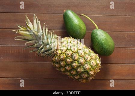 High-Angle Top View of a Whole Fresh Pineapple and Ripe Green Avocados on a Rustic Wooden Table Stock Photo