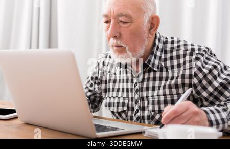 Mature man using laptop and writing in notepad Stock Photo