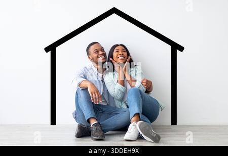 Excited african american spouses sitting near white wall with drawn house Stock Photo