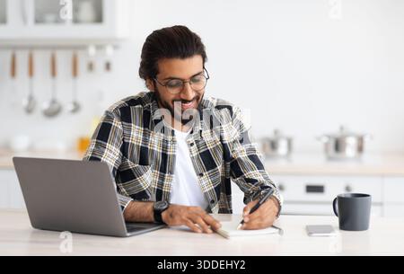 Positive arab guy looking for job online, kitchen interior Stock Photo