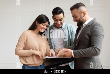 Three young adults reviewing documents together in a bright room Stock Photo
