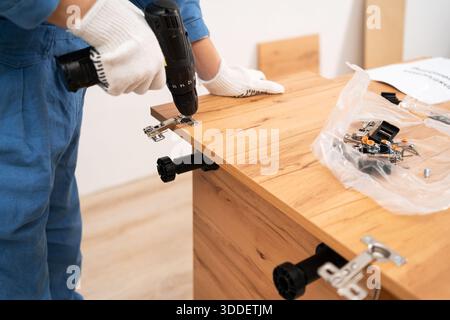 Close-up of female hands Installing a furniture door hinge using a power drill screwing hole. Stock Photo