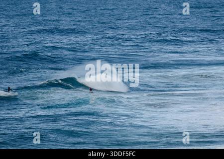 Surfers ride powerful ocean waves as a second rider paddles nearby in blue sea Stock Photo