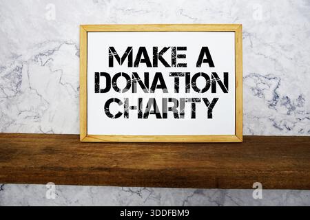 Make a Donation Charity text written on whiteboard with wooden shelf and marble background Stock Photo