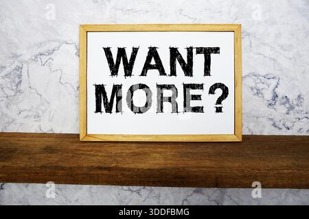 Want More? text written on whiteboard with wooden shelf and marble background Stock Photo