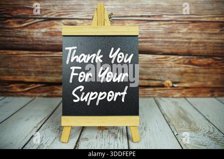 wooden easel holds a blackboard with the white text "Thank You For Your Support" set against a rustic wooden wall and light-colored wooden floor Stock Photo