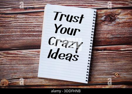 Trust Your Crazy Ideas text written on notepad top view on wooden background Stock Photo