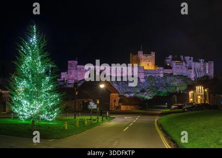 A view at night at Christmas at Bamburgh Village in Northumberland with Bamburgh Castle floodlit and Christmas decorations in the village square Stock Photo